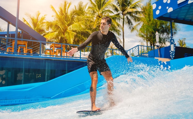 写真 水上遊園地で波シミュレーターでサーフィンをしている若い男性