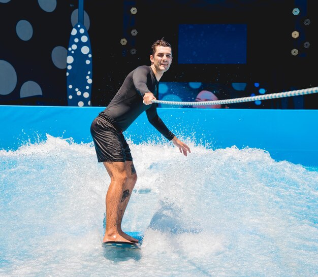 水上遊園地の波シミュレーターでトレーナーと一緒にサーフィンをしている若者