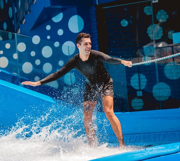 Young man surfing with trainer on a wave simulator at a water amusement park