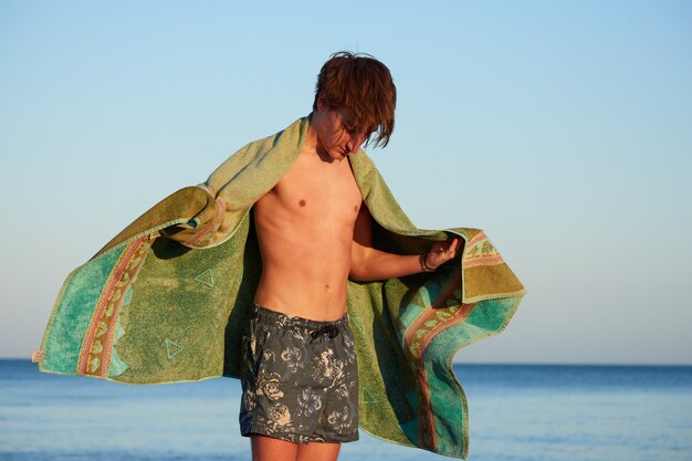 The young man in the swimsuit drying himself with the towel.