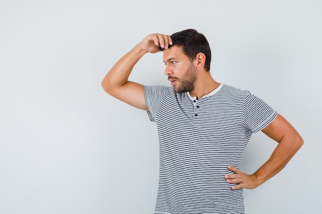 Young man in t-shirt looking away with hand over head and looking pensive , front view.