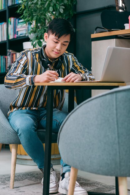 Young man at the table in coworking center smiling while making notes