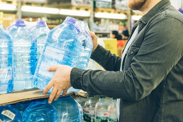 Young man take water from the shelf of the store