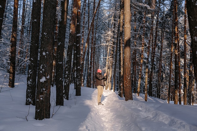 若い男は冬の森で写真を撮ります。新雪