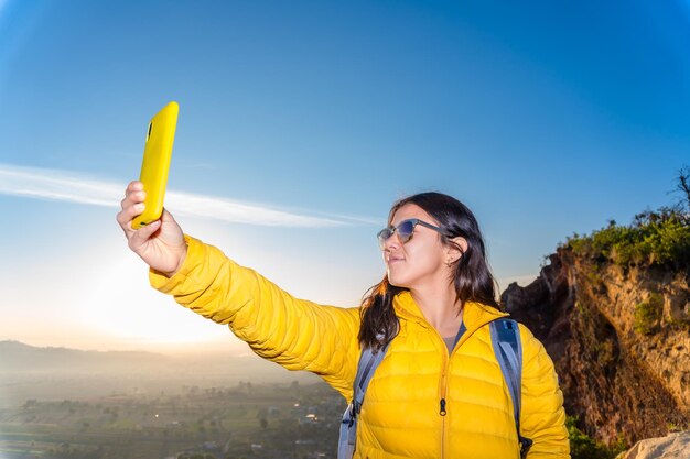 写真 山の頂上でスマートフォンでセルフィーを撮っている若い男