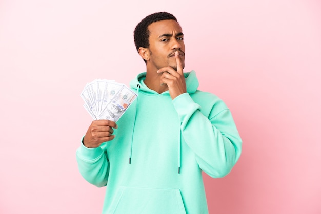 Young man taking a lot of money over isolated pink background having doubts while looking up