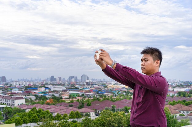 彼の携帯電話で街並みの写真を撮っている若い男