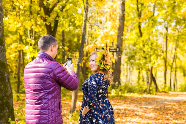 Young man taking photo of her girlfriend with mobile phone in autumn nature.