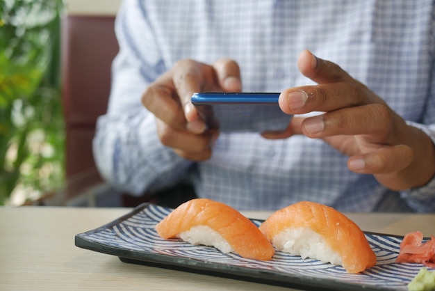 Фото Молодой человек фотографирует японского суши-лосося нигири с телефоном