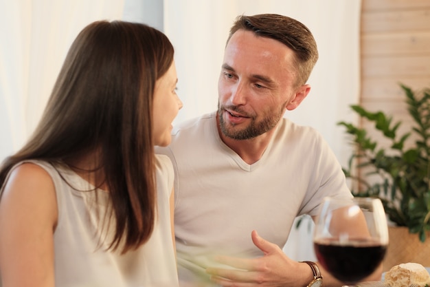 Молодой человек разговаривает со своей женщиной за столом во время ужина