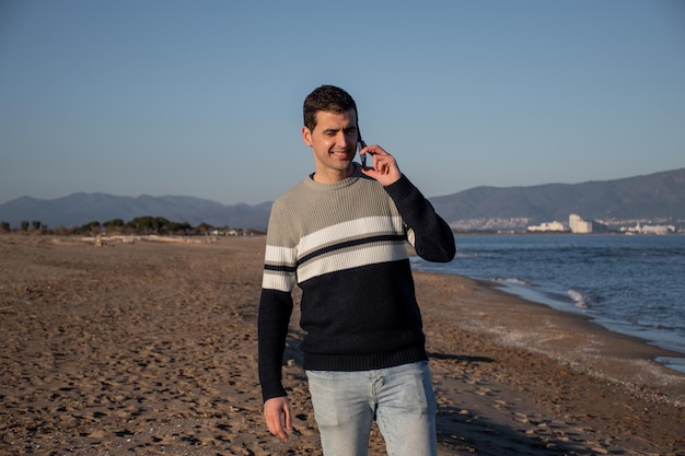 Young man talking on mobile phone on the beach during sunset