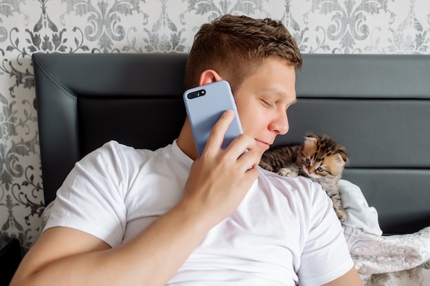 Young man talking on the phone and looking at cute kitten
