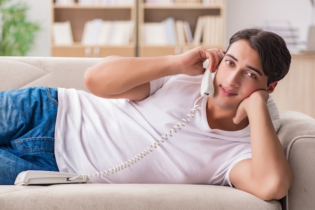 Молодой человек разговаривает по телефону, лежа в диване