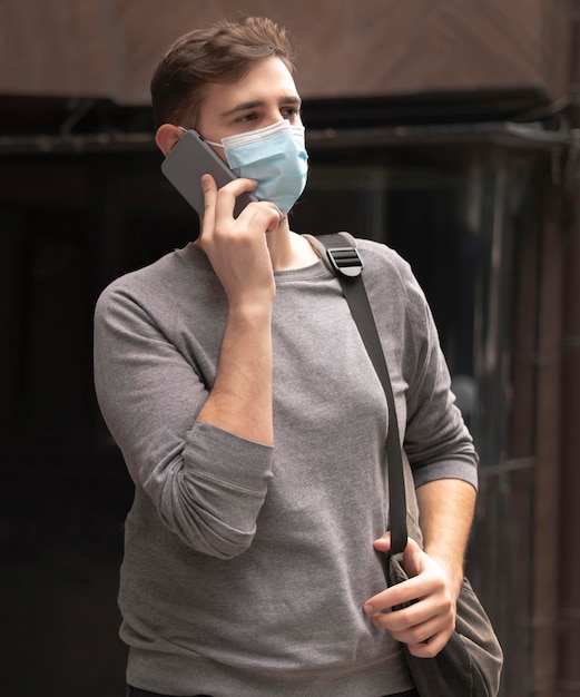 Photo young man talking on the phone outside while wearing a medical mask