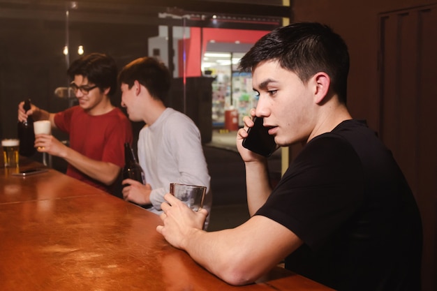 A young man talking on the phone while his friends enjoy a beer at the bar.