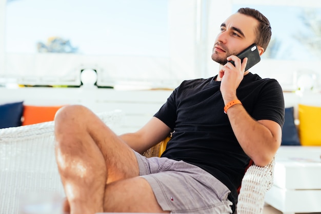 Young man talking a smartphone on the terrace by the sea. .