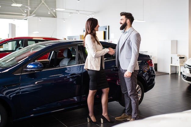 Photo young man talking with sales woman and choosing a new car at car showroom