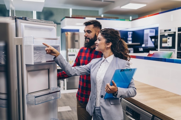 Young man talking with saleswoman about refrigerator he wants to buy.