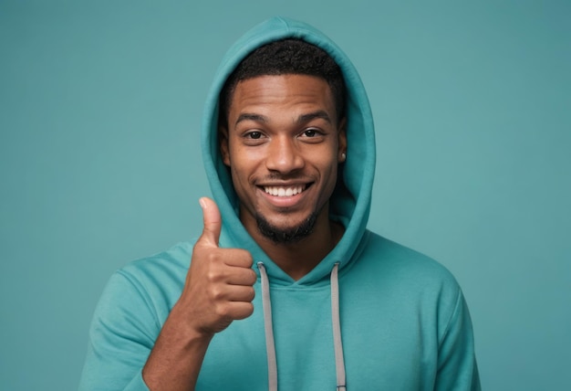 A young man in a teal hoodie gives a thumbs up with a bright smile against a matching teal