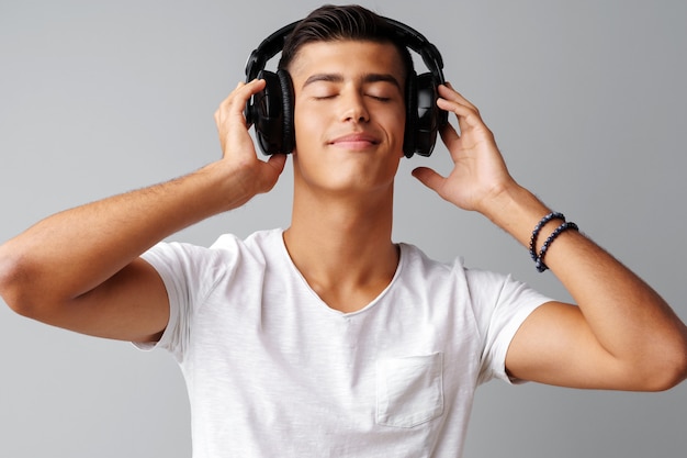 Adolescente del giovane che ascolta la musica con le sue cuffie sopra un fondo grigio