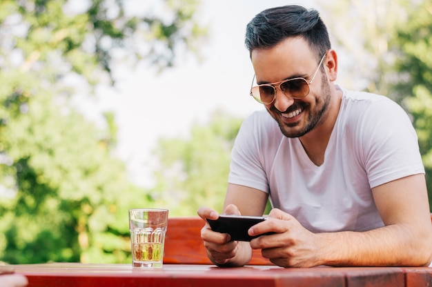 Foto giovane che manda un sms sul suo smartphone nel caffè della città