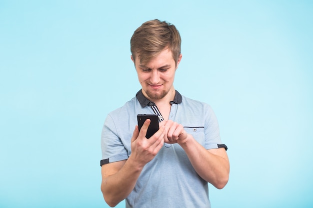 Young man texting message on smart phone isolated on blue