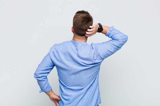 Photo young man thinking or doubting, scratching head, feeling puzzled and confused, back or rear view