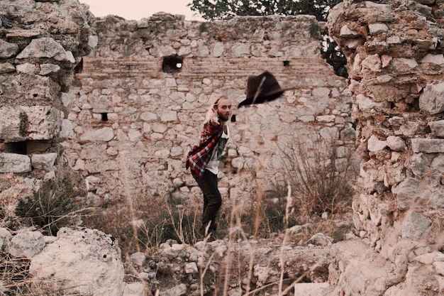 Foto giovane che lancia il cappello mentre è in piedi contro un muro abbandonato