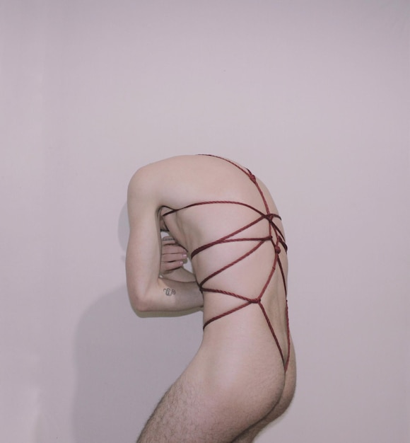 Young man tied up with rope standing against wall