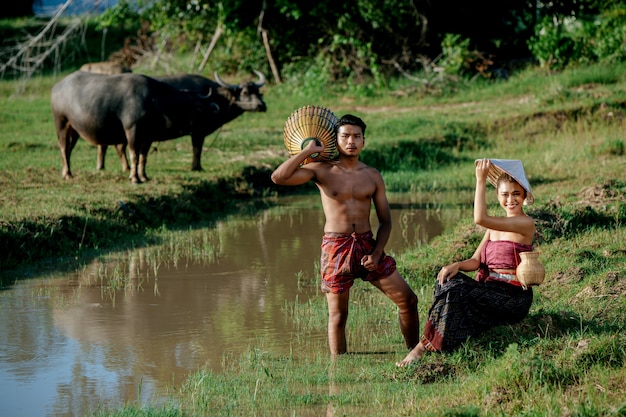 Giovane uomo in topless in piedi e tenendo in mano una trappola da pesca in bambù per pescare pesce per cucinare con una bella donna seduta vicino alla palude