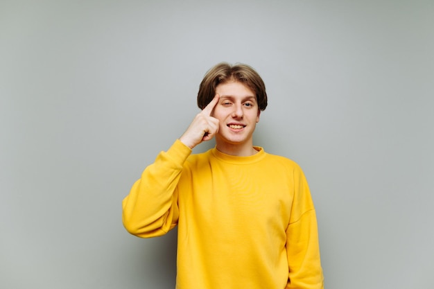 young man touches his finger to his temple and smiles