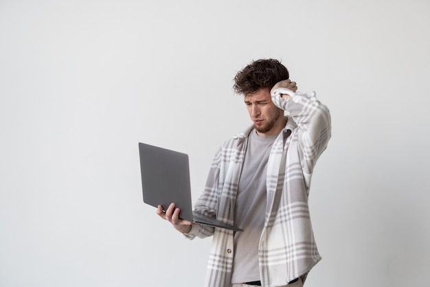 A young man touches his head wile working on his laptop on white background