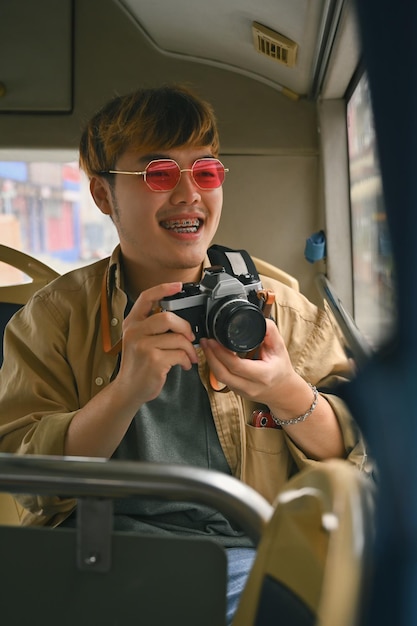 Young man tourist in pink glasses holding camera enjoying the travel on bus