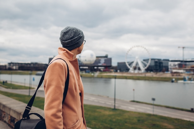 Young man tourist walking along pier by Wisla river in Krakow, Poland enjoying Ferris wheel landscape.