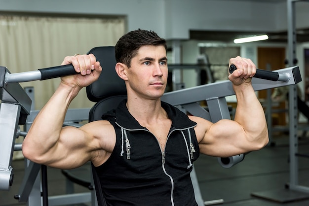 Young man training at sportive equipment in gym