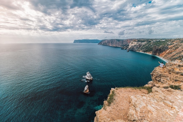 Young man traveler enjoys autumn seascape with overcast sky and volcanic coastline calm sea on a