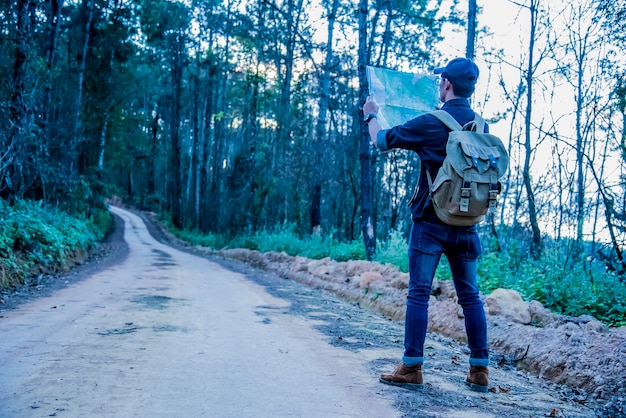Молодой человек путешественник с картой рюкзак, расслабляющий на открытом воздухе с каменистыми горами на фоне Летние каникулы и стиль жизни походы концепции