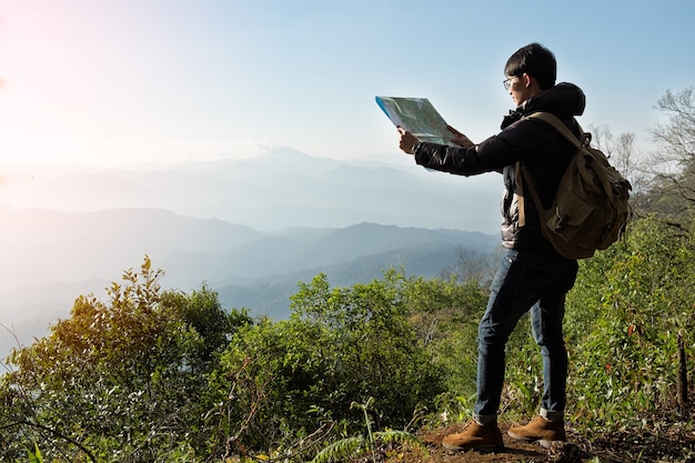 Young Man Traveler with map backpack relaxing outdoor with rocky mountains on background Summer vacations and Lifestyle hiking concept