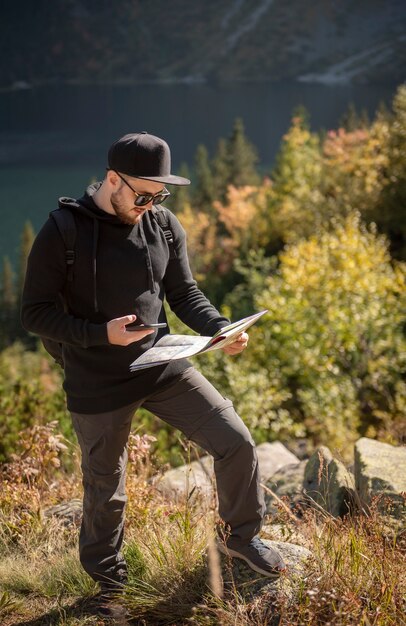 Young man traveler with map and backpack relaxing outdoor with rocky mountains on background