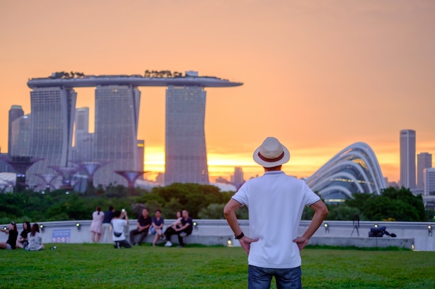 Young man traveling with hat at Sunset, solo Asian traveler visit in Singapore city downtown. landmark and popular for tourist attractions. Asia Travel concept