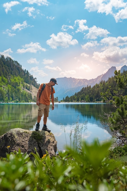 緑の山の頂上をトレッキングする若い男は、日没時に素晴らしい風景の景色を楽しんでいます