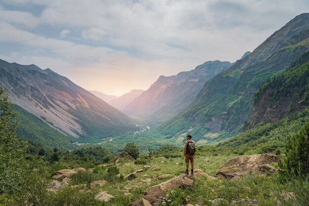 Young man trekking on the top of a green mountain during sunset