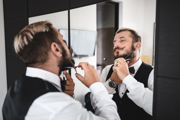 Young man trims his beard with scissors