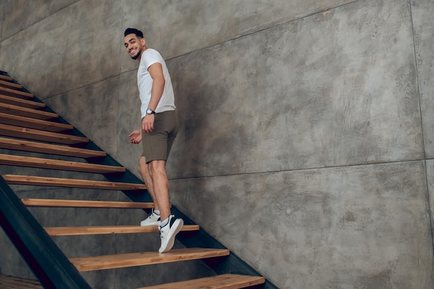 A young man in tshirt and shorts on the stairs at home