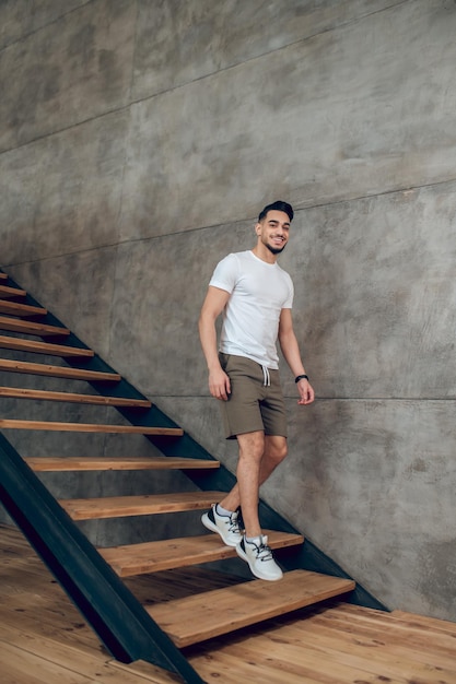 A young man in tshirt and shorts on the stairs at home