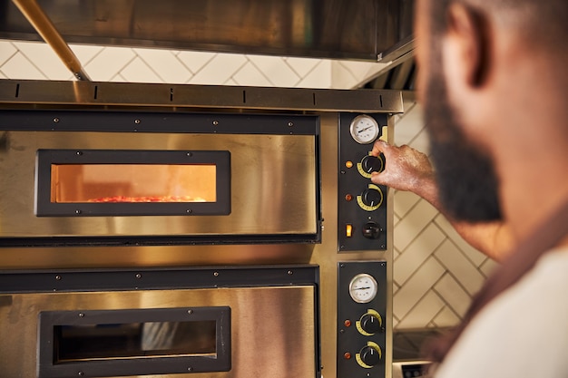 Foto giovane che accende il forno e imposta la temperatura per la cottura del piatto