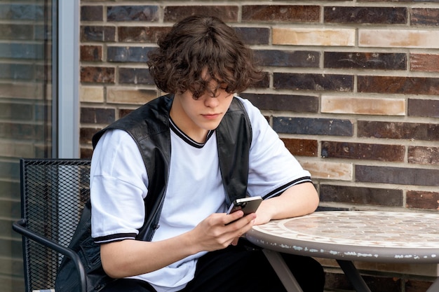 Young man typing something on the phone while sitting at an outdoor cafeteria table