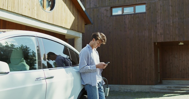 庭に立って車に寄りかかっている若い男が携帯電話を使っている
