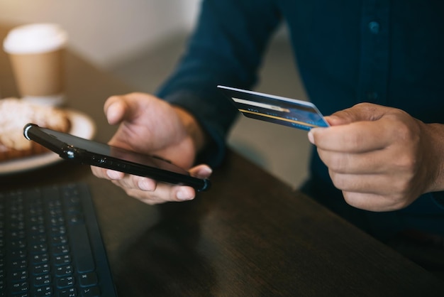 Young man uses a smartphone to shop online with a credit card at an indoor coffee shop