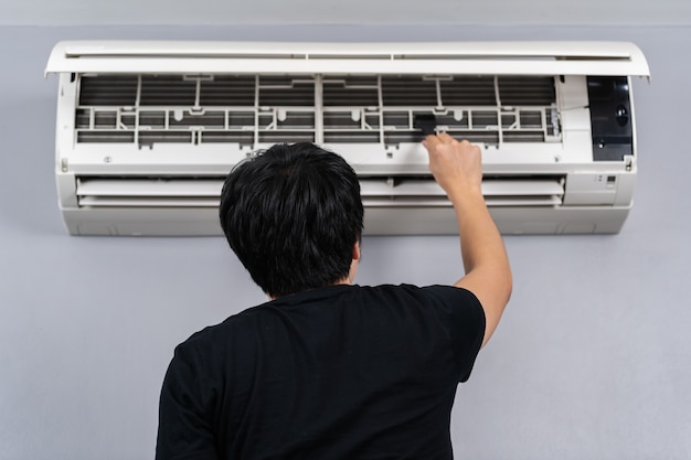 Young man using brush to cleaning the air conditioner indoors at hone